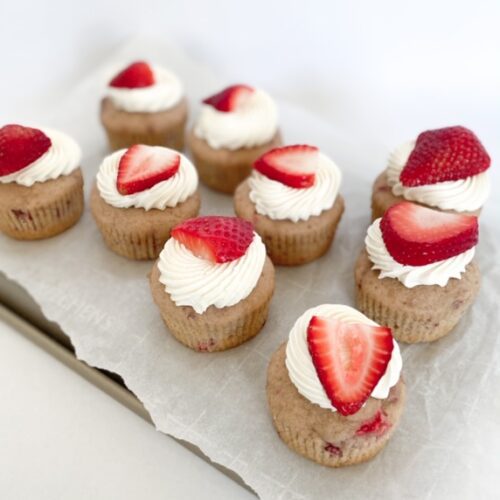 strawberry cupcakes with white icing and sliced strawberry on top with a white background.
