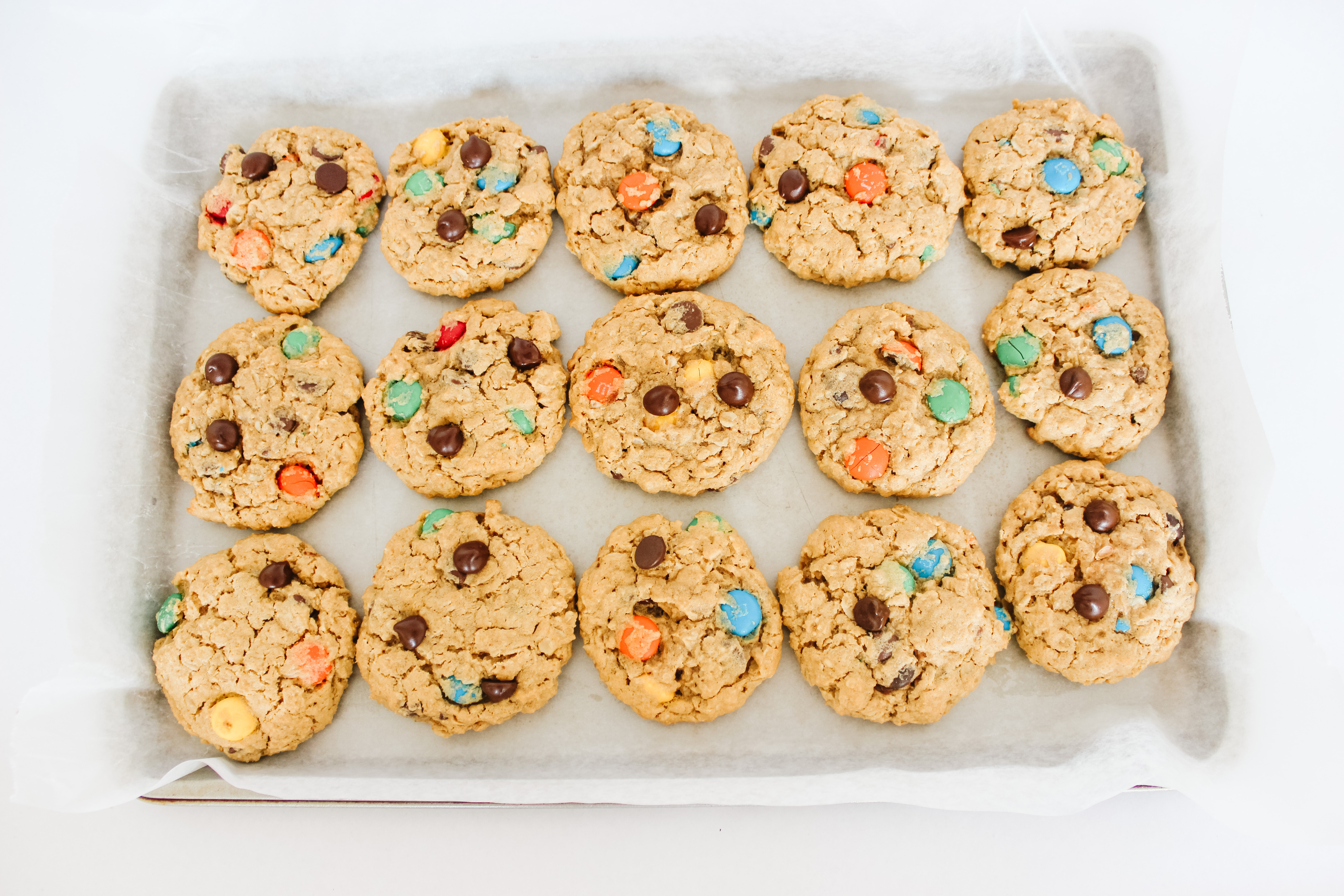 15 monster cookies on parchment paper and pan with a white background