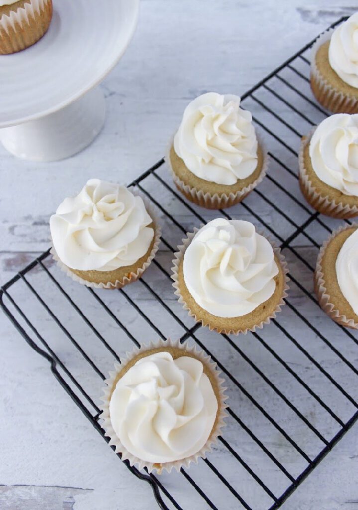 Almond Cupcakes on a cooling off rack with a white wood background
