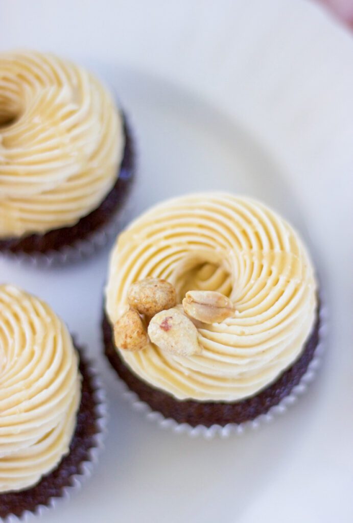Peanut Butter Chocolate Cupcake with light yellow frostings and nuts on top with a white background.