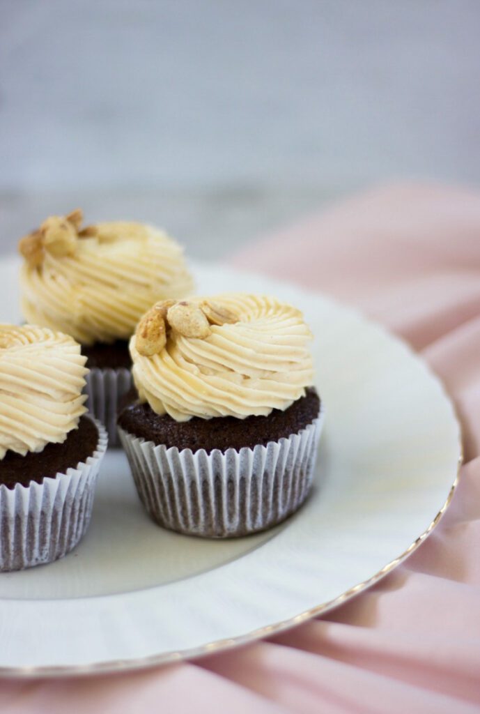 Peanut Butter Chocolate Cupcake with frosting and nuts on top on a white a gold plate.