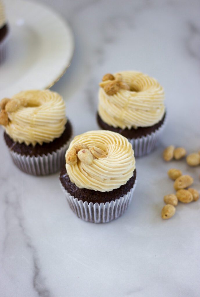 Peanut Butter Chocolate Cupcakes with nuts next to them on a white marble counter.