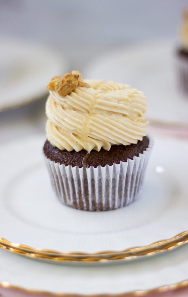 Peanut Butter Chocolate Cupcake with frosting and nuts on top on a white a gold plate.