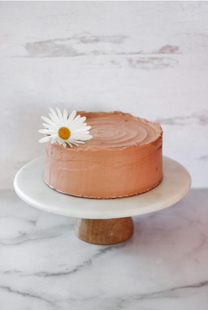 Chocolate Zucchini Cake with a flower on top and on a white cake stand