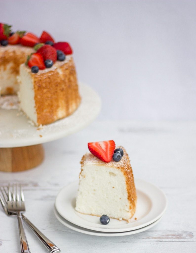a slice of Delicious Easy Angel Food Cake  with blueberries and strawberries on top with a white background.