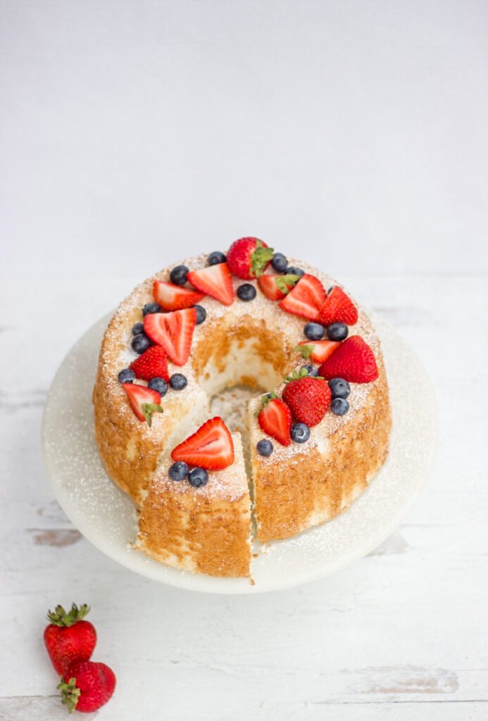 Delicious Easy Angel Food Cake  with blueberries and strawberries on top with a white background.