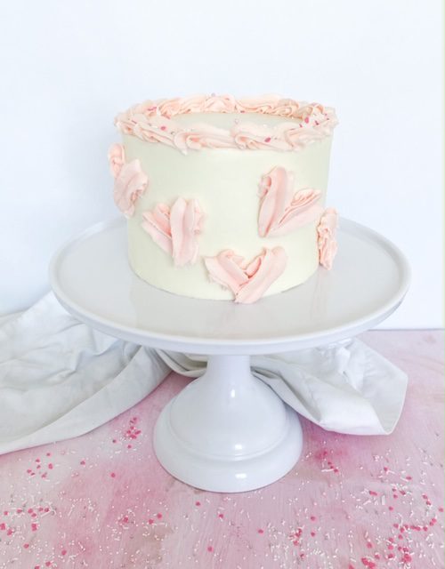 Earl Grey Cake with white and pink frosting on a white cake stand and white and pink background.