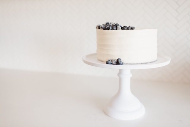 Lemon Blueberry Cake with white frosting and blueberries on it with a white background.